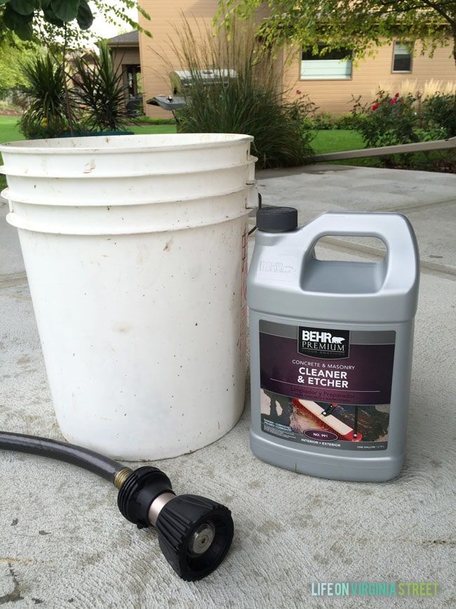 a white bucket sitting next to a black hose on top of a cement floor near a gallon of cleaner