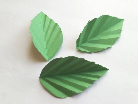 three pieces of green paper with leaves cut out of them sitting on a white surface