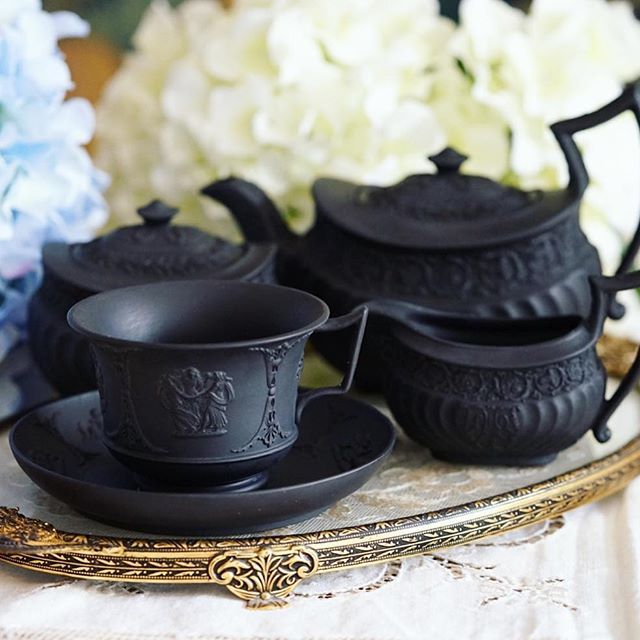 three black tea cups and saucers sitting on a tray with flowers in the background