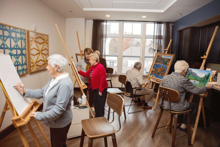 an older woman is painting while others look on