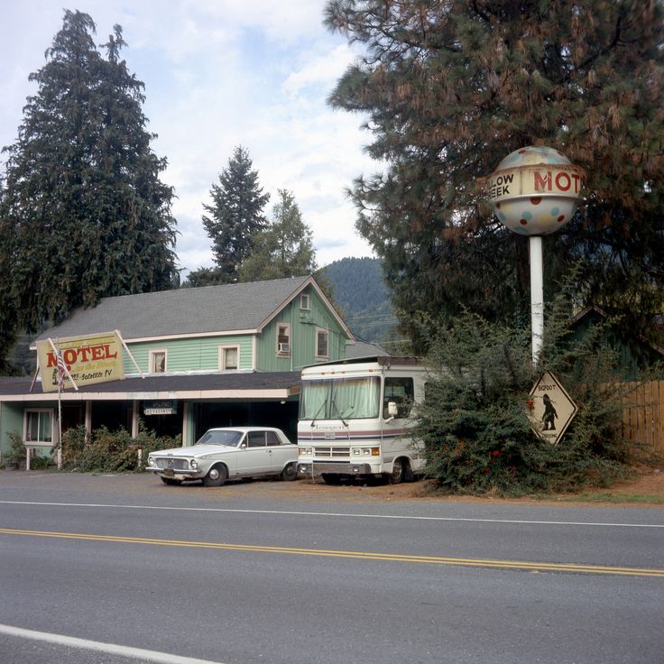 an rv parked in front of a motel next to a street sign and pine trees