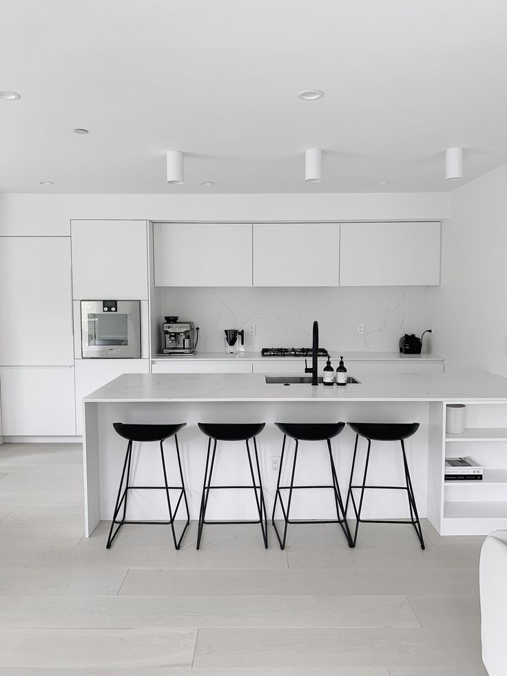 a white kitchen with three stools in front of the counter top and an island