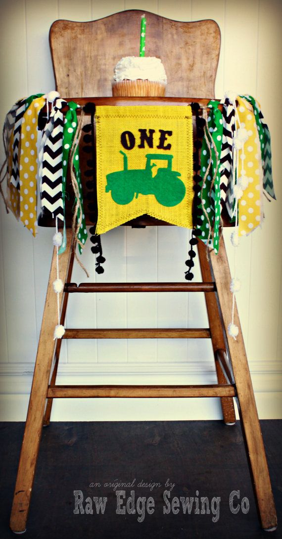 a wooden high chair with a green and yellow one birthday banner hanging from it's back