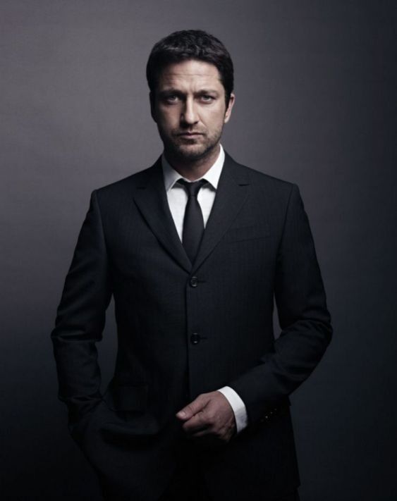 a man in a black suit and tie posing for a photo with his hands in his pockets