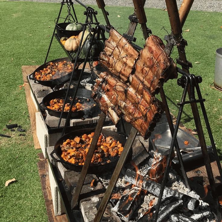 food is being cooked on an outdoor grill in the grass near a fire pit and picnic table