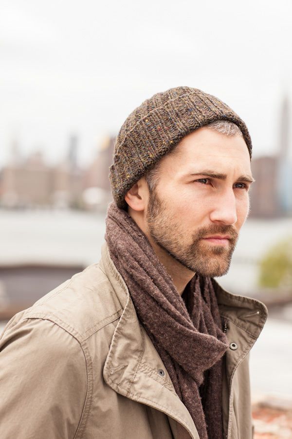 a man wearing a hat and scarf looking off into the distance with a city in the background