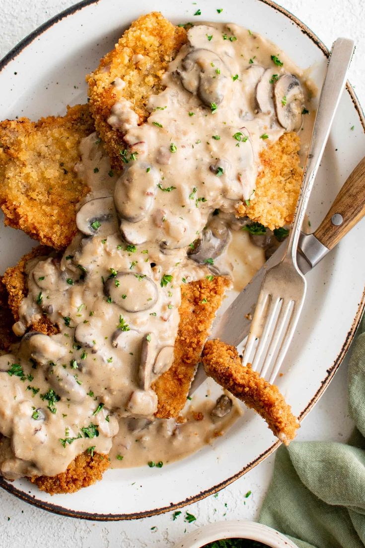 a white plate topped with fried chicken covered in mushroom gravy and two forks