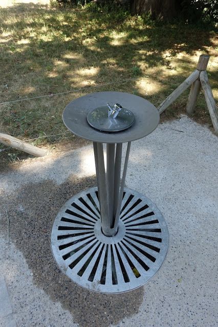 a metal table sitting on top of a cement ground next to a tree trunk and grass