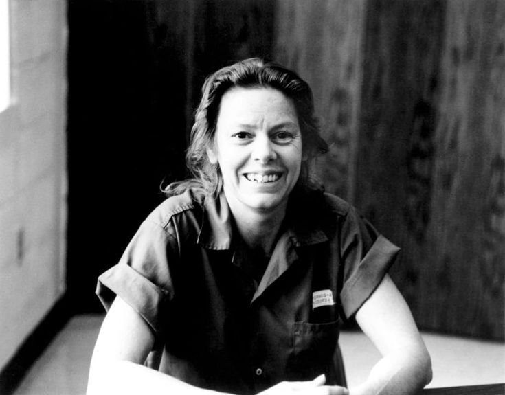 a black and white photo of a woman sitting in front of a wooden door smiling