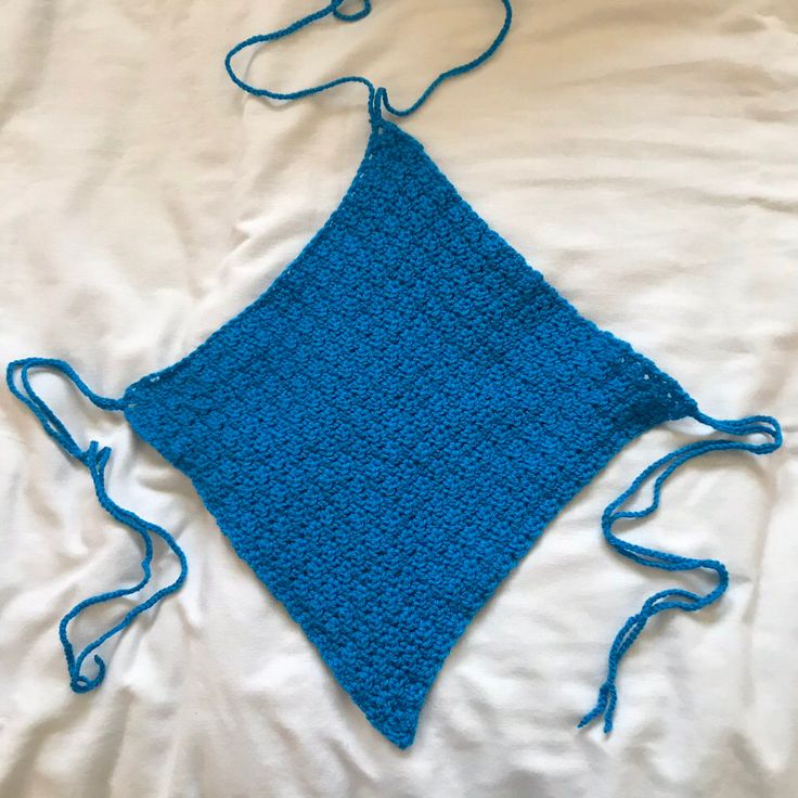 a blue crocheted square on top of a white sheet with a hook in the middle