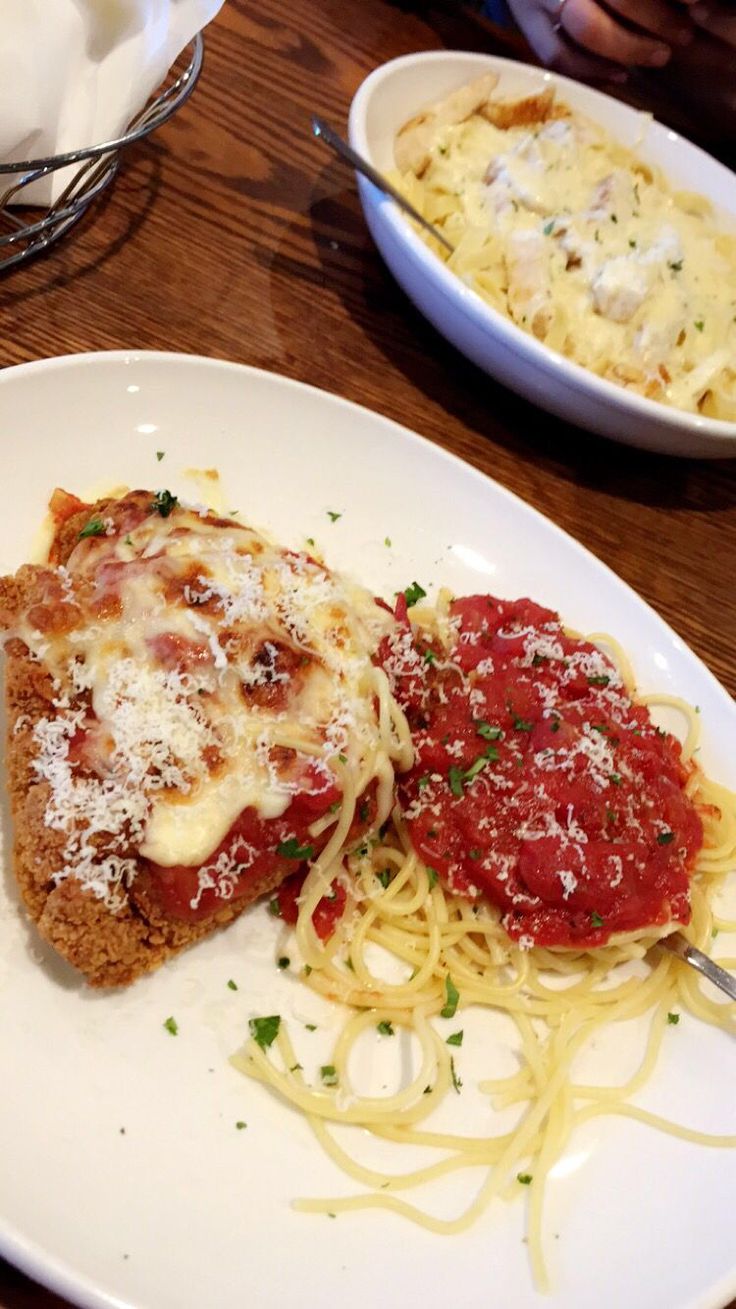 two plates of food on a table with pasta and sauces in the bowl behind them