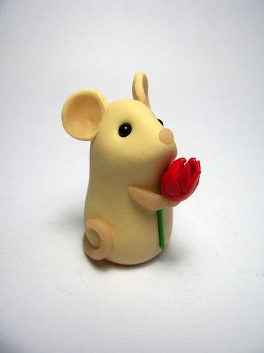 a toy mouse holding a red flower on a white surface with one eye open and the other half closed