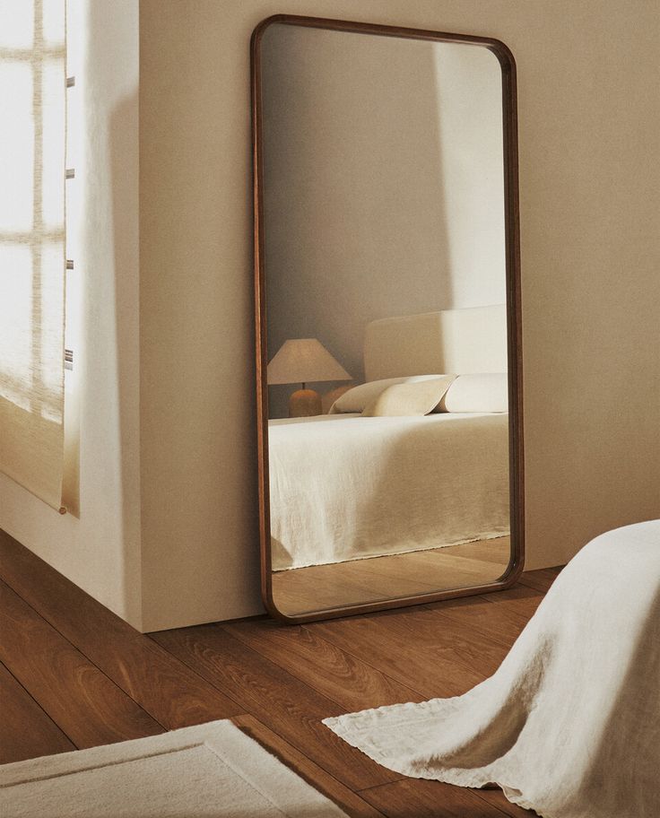 a large mirror sitting on top of a wooden floor next to a white bed in a bedroom