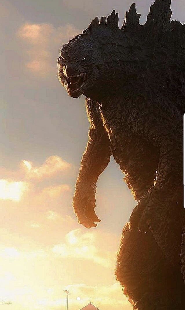 a giant godzilla statue with the sun setting in the background