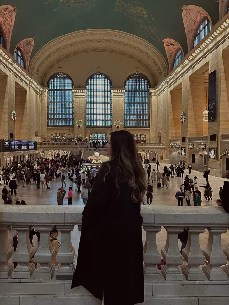 a woman is looking at the ceiling in a train station with many people walking around