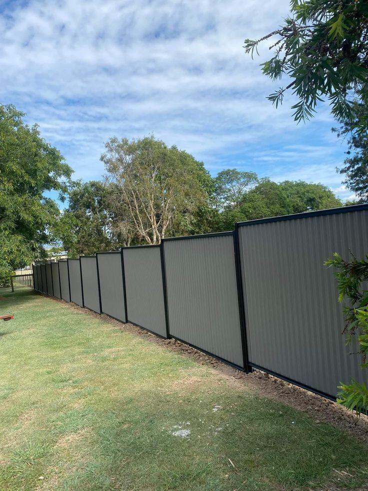 a fence that is in the middle of a yard with grass and trees around it