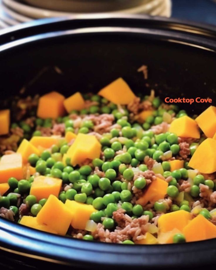 a close up of food in a crock pot with peas and cheese on top