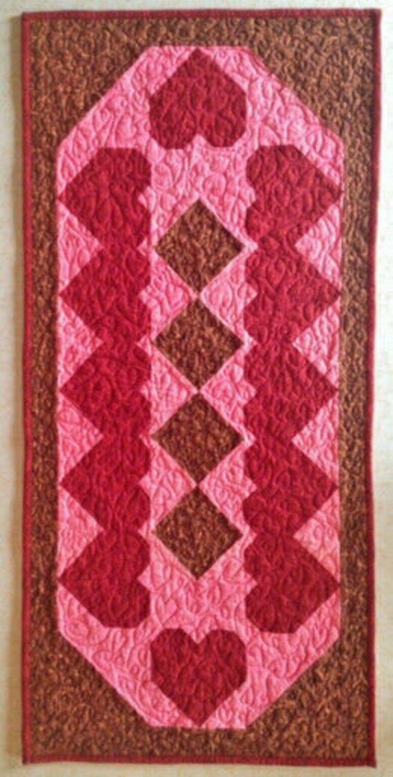 a pink and brown quilt hanging on the wall next to a white wall with a red border