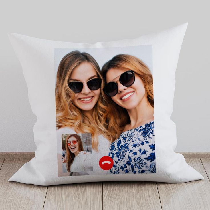 two women wearing sunglasses are smiling and posing for a photo on a pillow cover that is sitting on a wooden floor