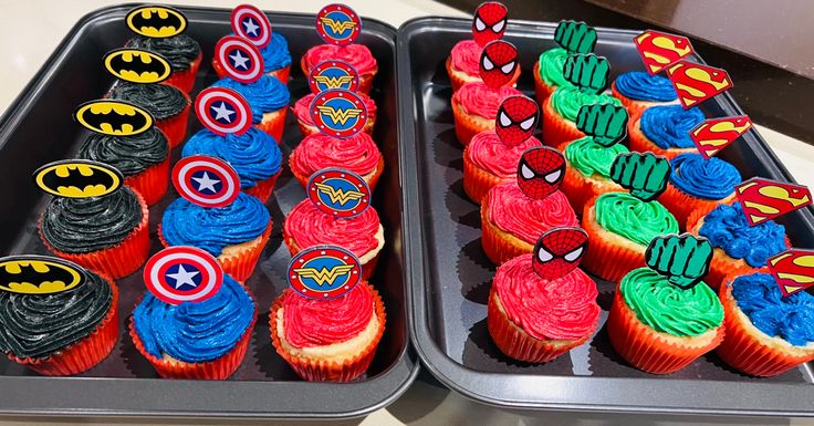 two trays filled with cupcakes covered in icing and decorated like superheros