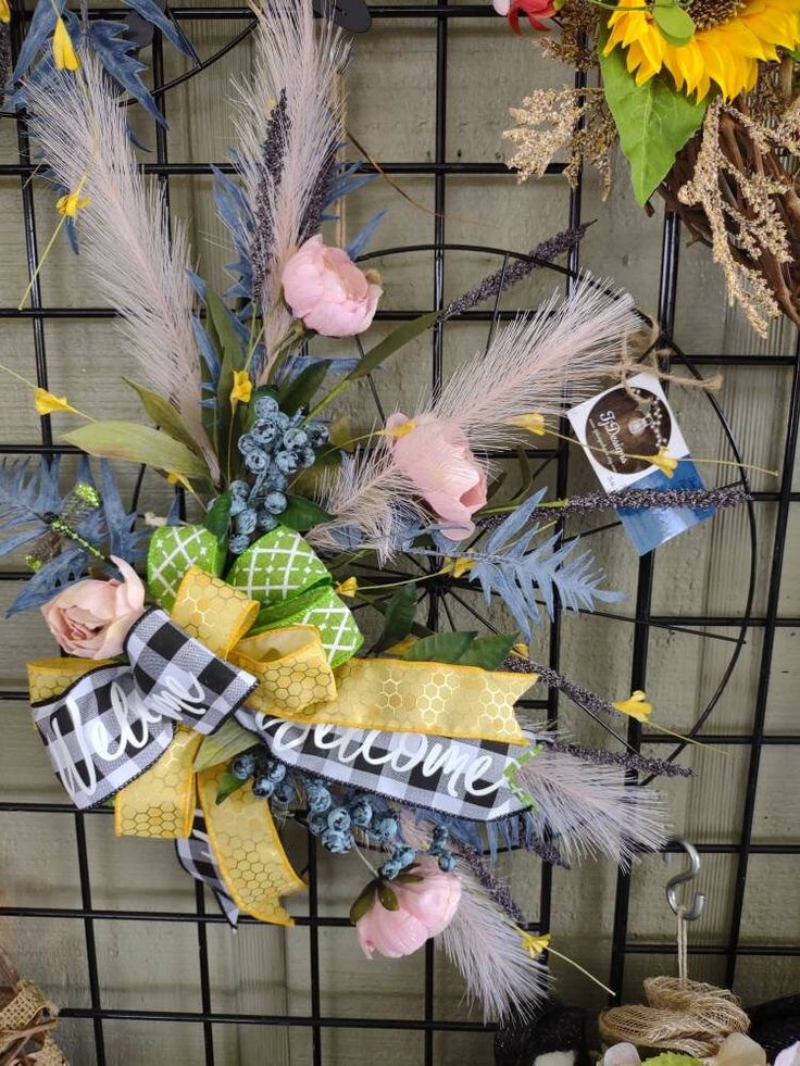 a wreath with flowers and ribbons hanging on a fence