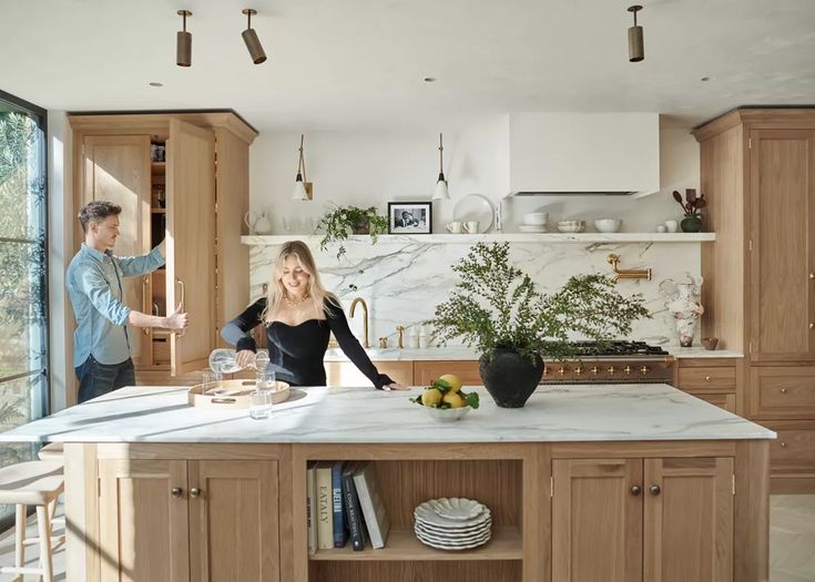 a man and woman standing in a kitchen next to an island with marble counter tops