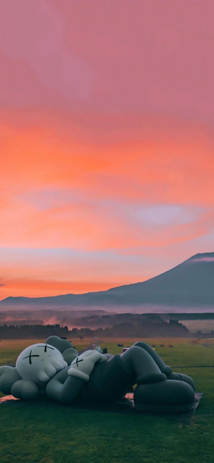 a large inflatable object laying on top of a lush green field under a pink sky