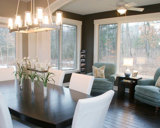 a dinning room table with chairs around it in front of two large windows that look out onto the woods