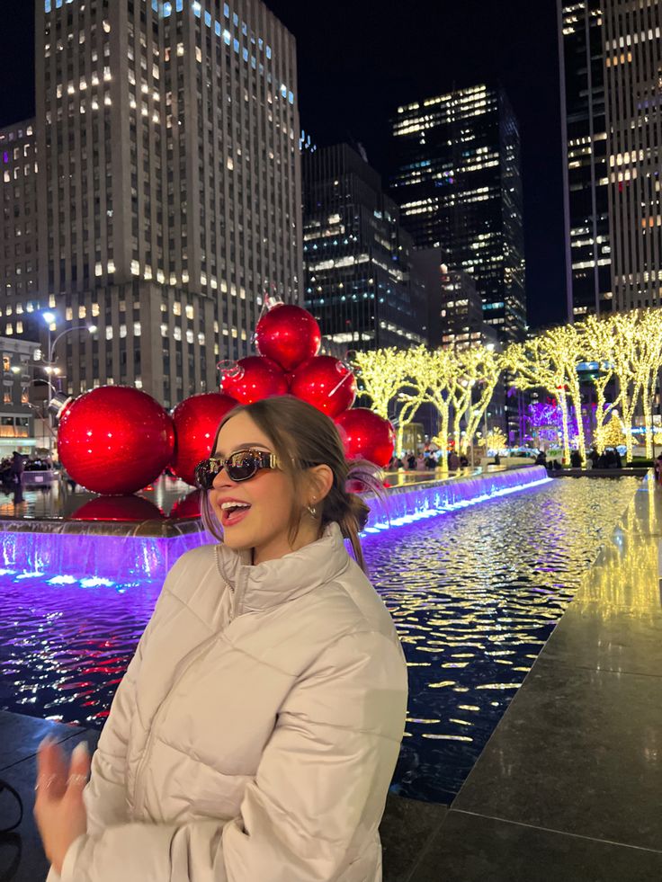 a woman standing in front of a fountain with red balls on it's head