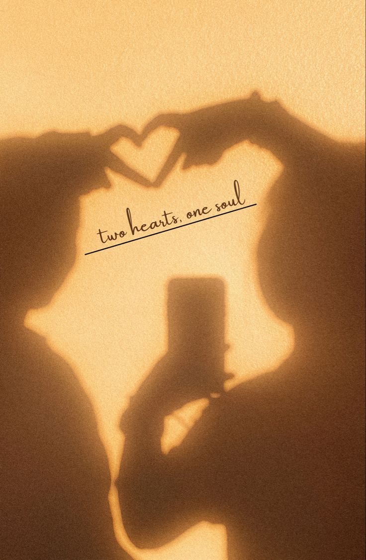 the shadow of two people making a heart with their hands and holding a small cup