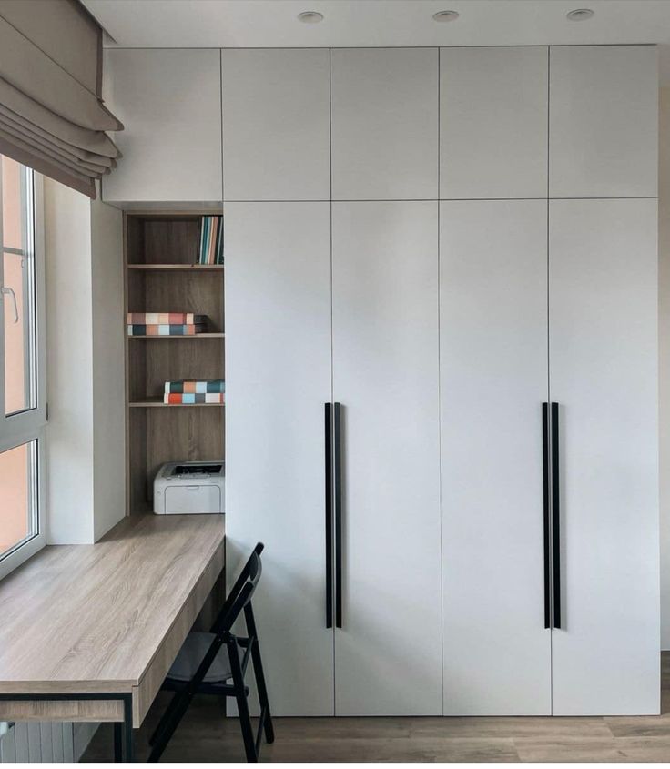 a kitchen with white cupboards and wooden flooring next to a window in the room