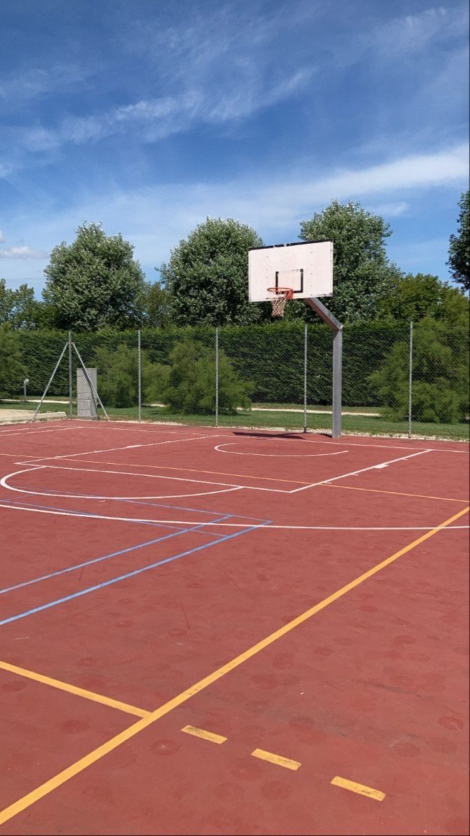 an empty basketball court with yellow lines and trees in the background on a sunny day