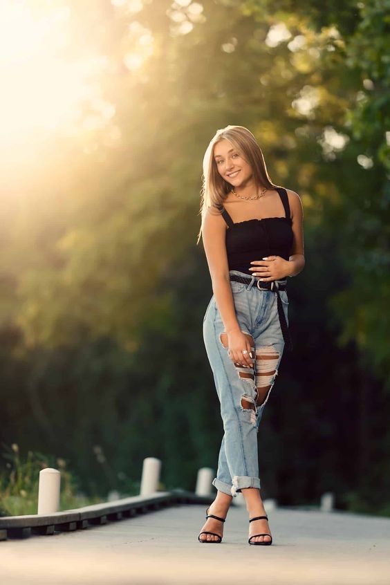 a woman in ripped jeans and black top posing for the camera with her hand on her hip