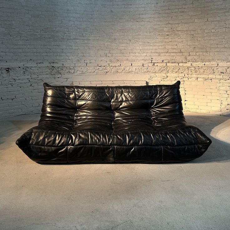 a black leather futon sofa sitting in front of a white brick wall and floor