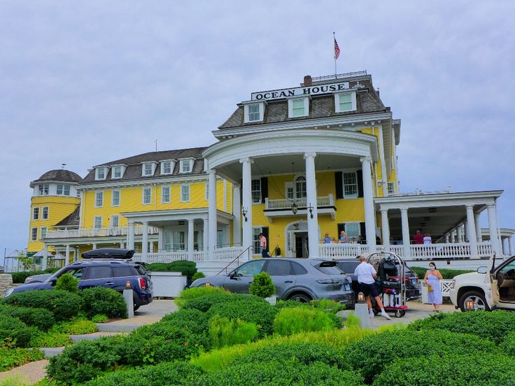 several cars parked in front of a large yellow building with people standing on the porch