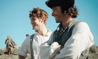 two young men standing next to each other on a hill with people in the background