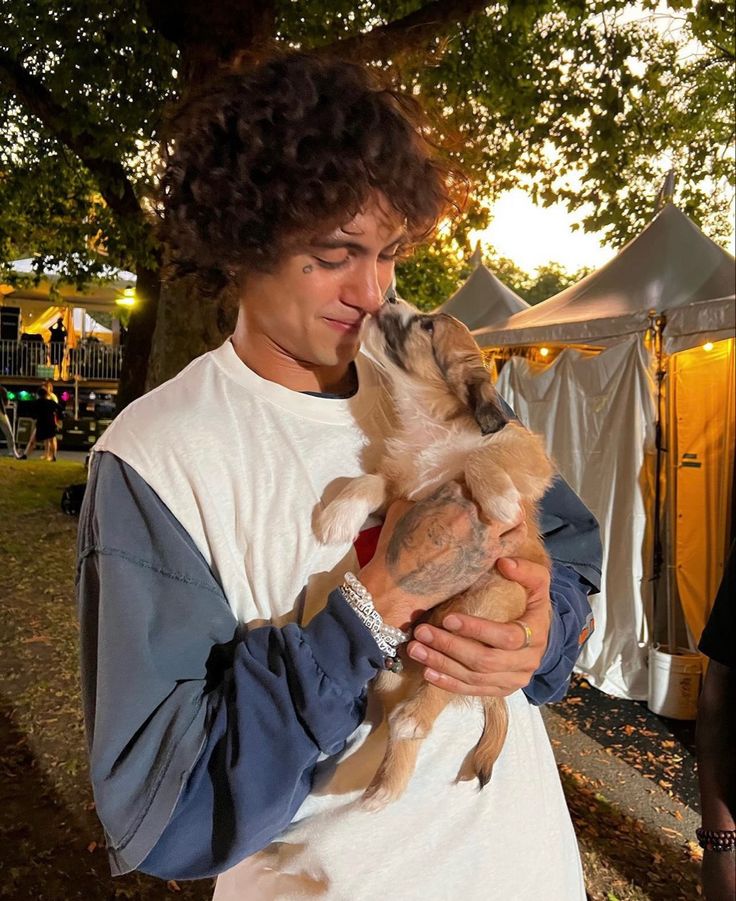 a young man holding a small dog in his arms at an outdoor event with tents behind him