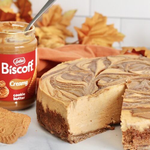 a cheesecake with a slice missing from it next to a jar of biscott cream