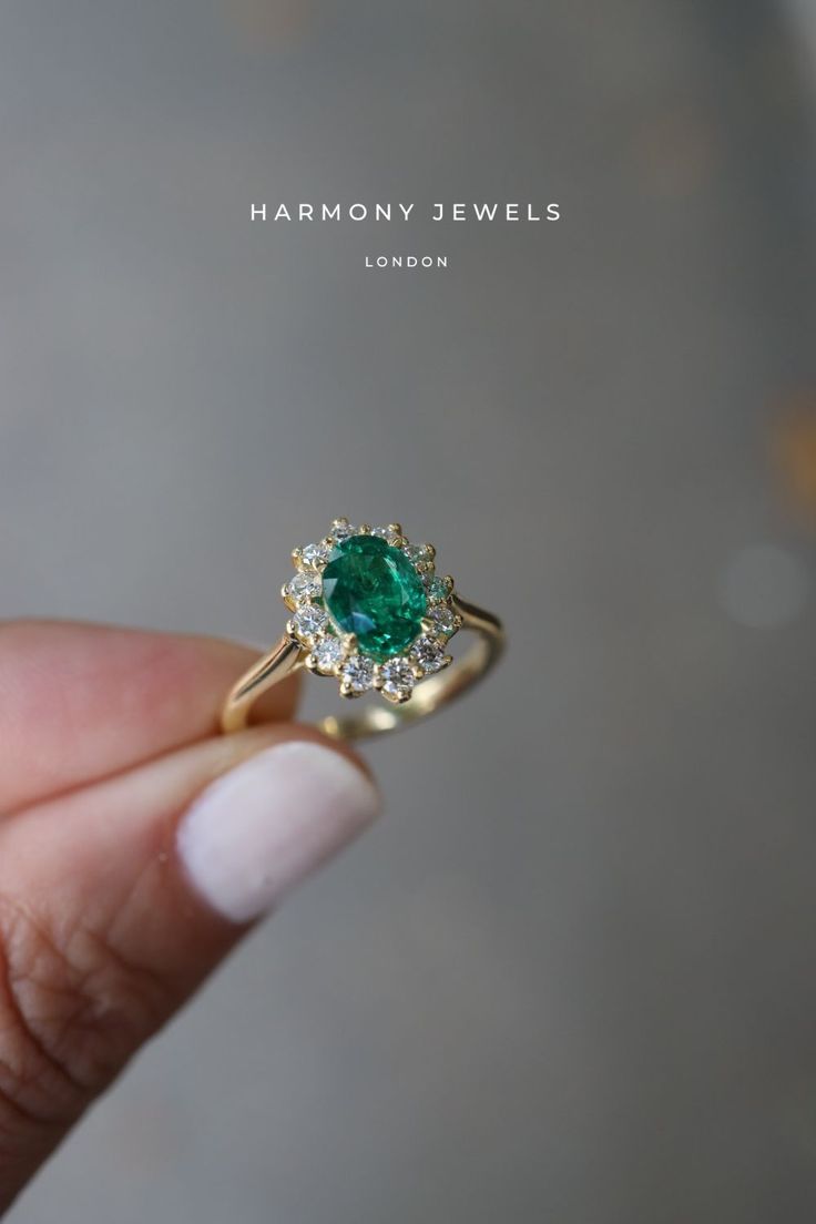 a close up of a person's hand holding an emerald and diamond ring