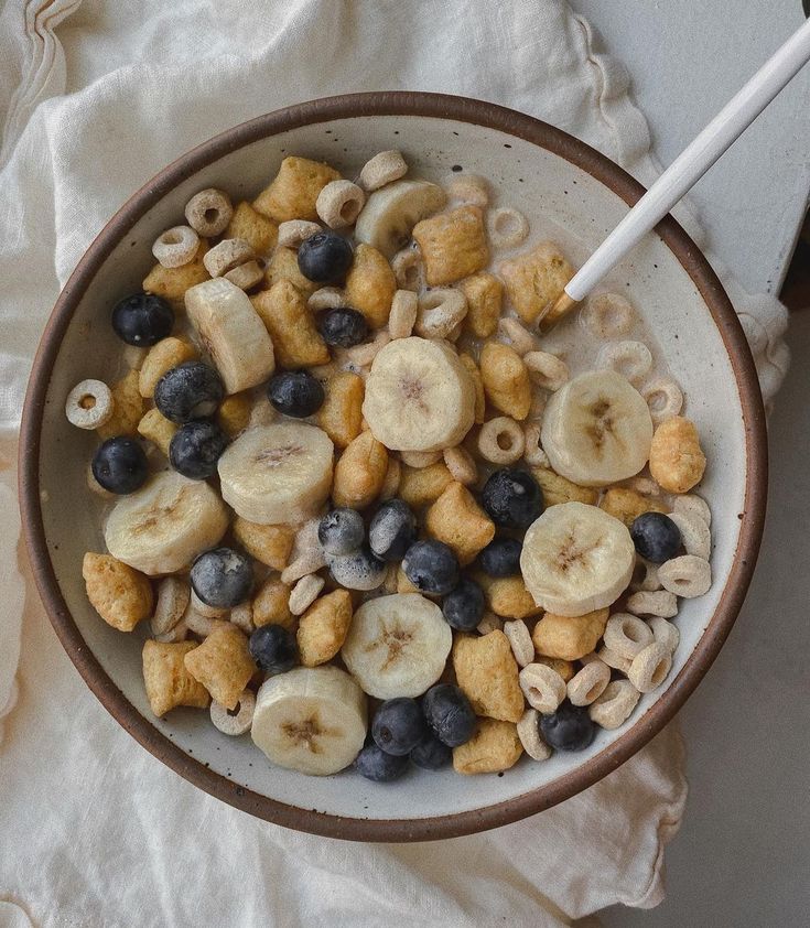 a bowl filled with cereal and blueberries on top of a white cloth next to a spoon