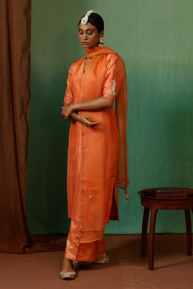 Rust orange silk kurta with placement vintage motif, contrast thread, zari, bead and sequin embroidered half sleeves. Paired with tissue stripe pattern straight pant and organza embroidered dupatta.
Components: 3
Pattern: Embroidered
Type Of Work: Sequin, Zari, Thread and Bead Work
Neckline: V Neck
Sleeve Type: Half Sleeves
Fabric: Kurta: Silk, Pant: Tissue, Dupatta: Organza
Color: Orange
Other Details: 
Tasselled dupatta edges
Beaded hem details
Lace work dupatta border
Side slits on kurta
Occa Tissue Dupatta, Dupatta Border, Silk Pant, Kurta Set For Women, Indian Dresses Traditional, Silk Kurta, Embroidered Dupatta, Rust Orange, Kurta Set