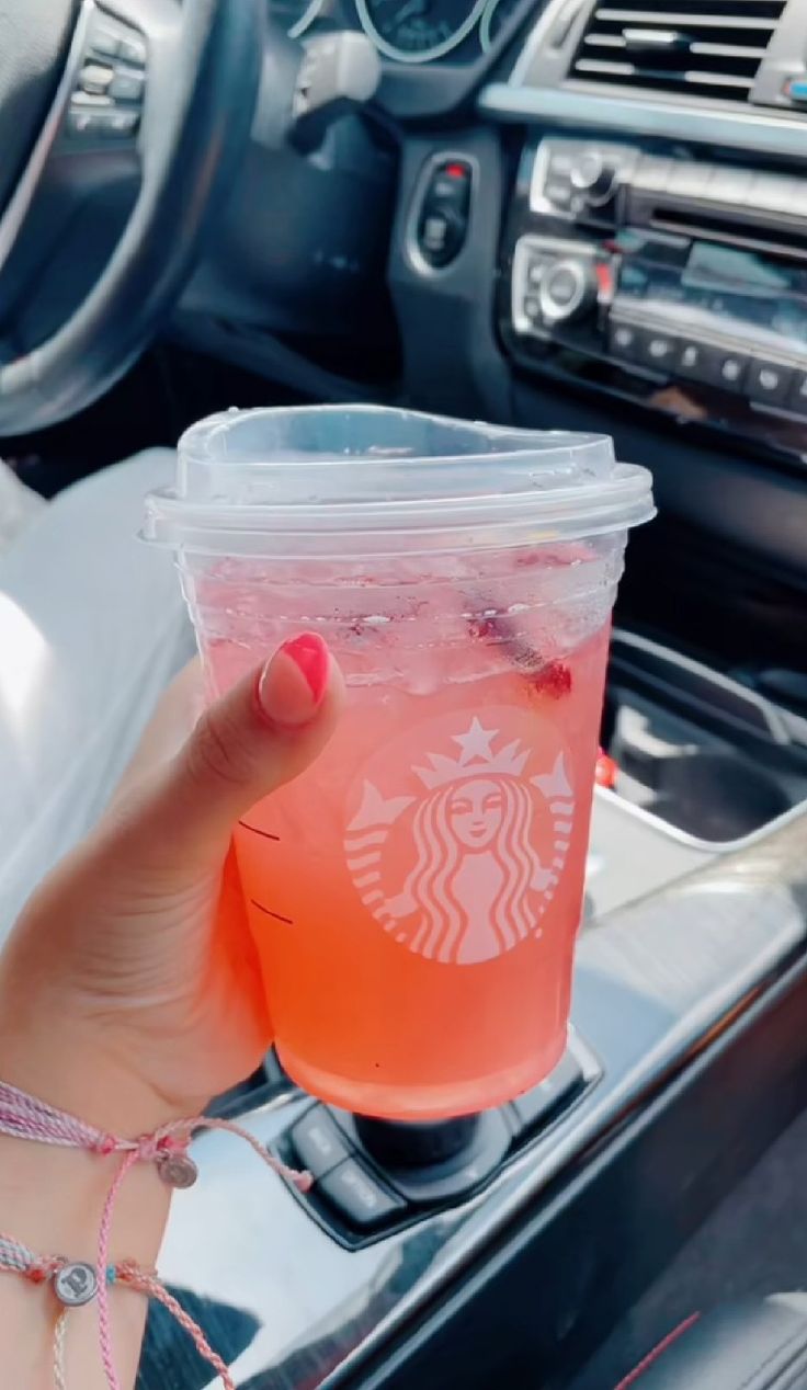 a woman holding up a cup of drink in her hand while sitting in the drivers seat of a car