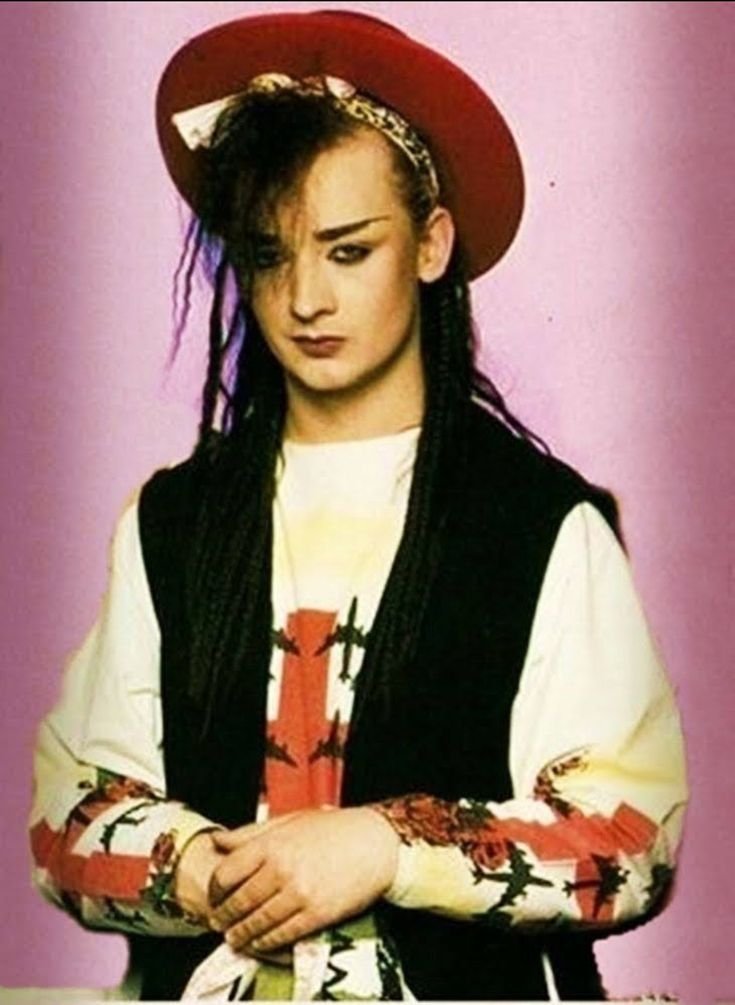 a woman with long hair wearing a red hat and black vest standing in front of a purple background