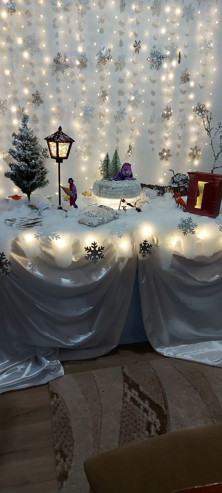 a table covered in snow with lights and decorations on the wall behind it is a christmas scene