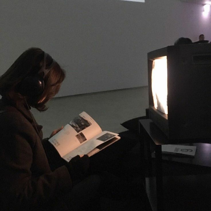 a woman sitting in front of a tv with headphones on while reading a book