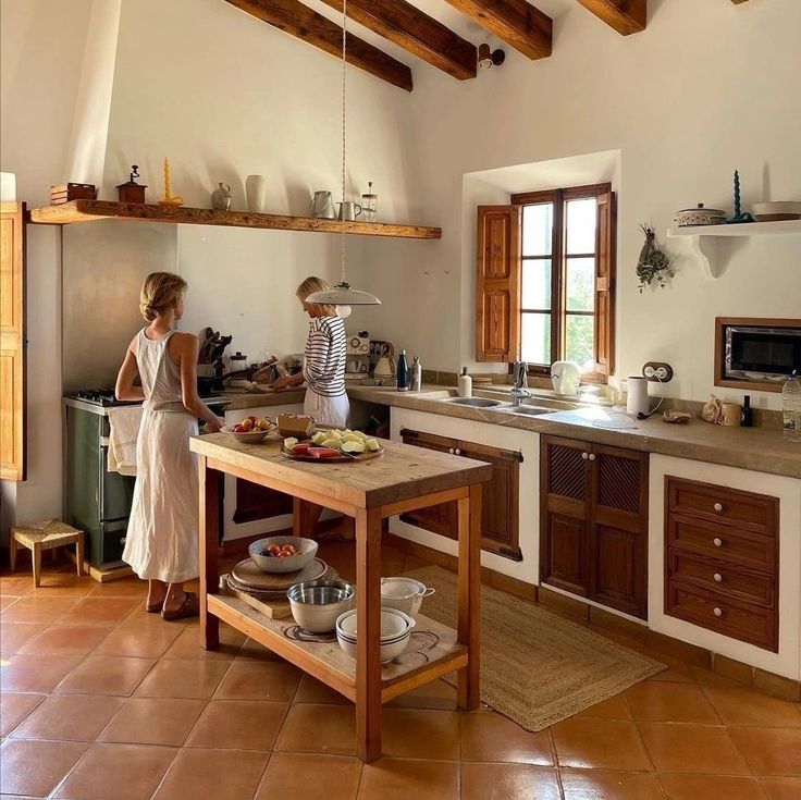 two people in a kitchen preparing food on a table and shelves above the stove top