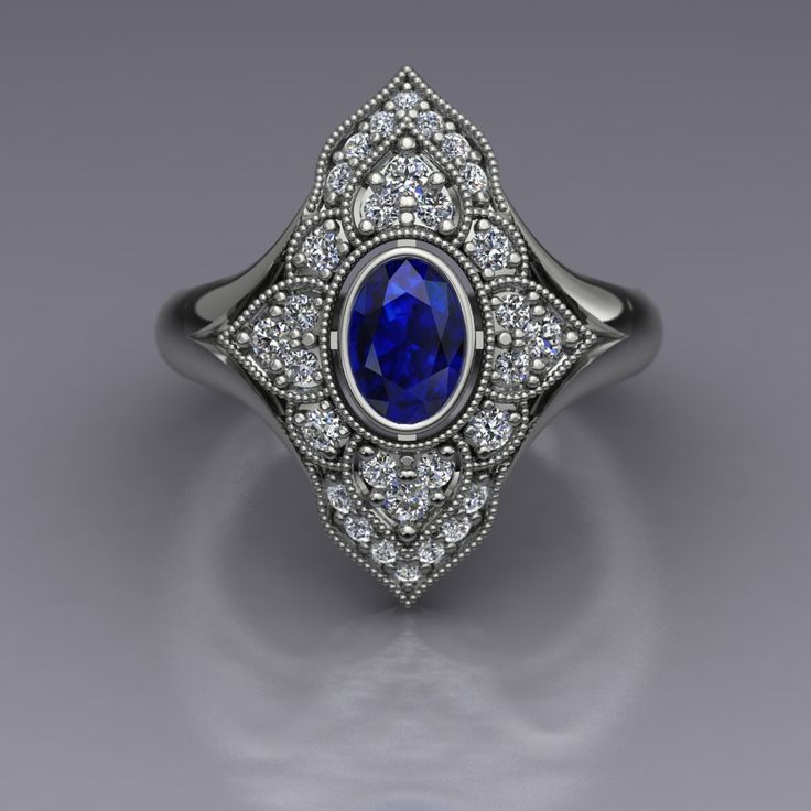 "An oval blue sapphire is set in a bezel in this diamond-studded dinner ring in 14k white gold. The vintage inspired diamond panels are edged with milgrain beading. The top of the ring measures about 20mm at the widest point. Blue Sapphire Dimensions6x4mm EnhancementHeated Carat Weight 0.70 ColorMedium to dark navy blue ClaritySlightly included CutGood PolishGood Diamonds Number22 EnhancementNatural Carat Total Weight0.29 ColorF-G ClaritySI1-2 CutVery Good PolishVery Good This is a custom made item! When you order, we will create a wax model of your ring with our 3D printer. This model is then cast in 14k gold, which is polished and set by hand. This process takes 3-4 weeks, so please allow for this time when ordering if your ring is for a special occasion. Your ring will arrive in a desig Art Deco Oval Sapphire Ring With Accent Stones, Art Deco Oval Diamond Ring With Accent Stones, Blue Oval Sapphire Ring In Art Deco Style, Classic Oval Sapphire Ring With Diamond Accents, Art Deco Blue Oval Sapphire Ring, Classic Oval Cabochon Sapphire Ring For Anniversary, Luxury Oval Sapphire Ring With Bezel Setting, Oval Sapphire Ring With Diamond Accents In White Gold, Oval Sapphire Ring In White Gold With Diamond Accents