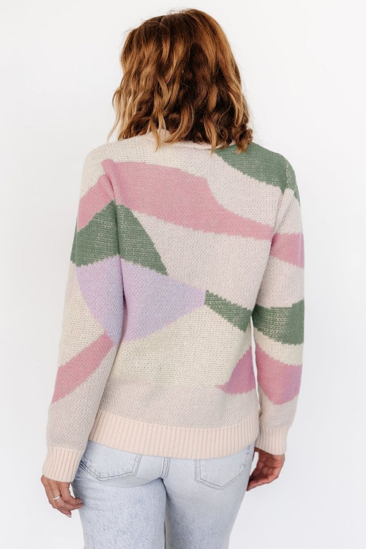 a woman wearing a pink, green and white sweater with geometric designs on the back