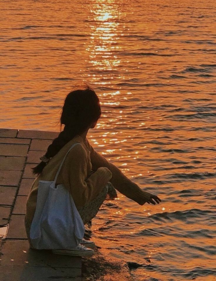 a woman sitting on the edge of a body of water