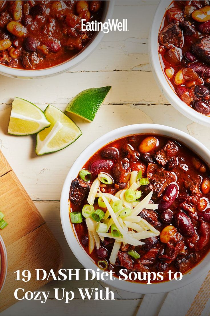 three bowls filled with chili and beans next to sliced limes on a cutting board